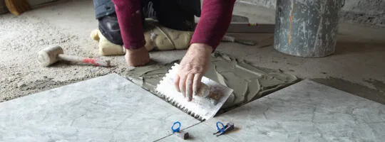 Close-up of a tile installer troweling adhesive before laying floor tile